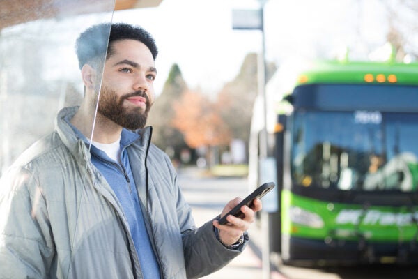 young man with beard holds phone while about to board the bus.