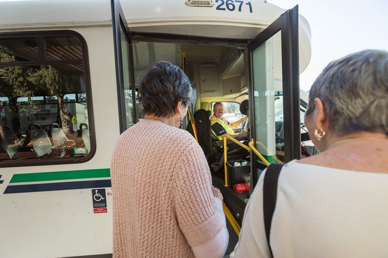 Two riders board a bus while the operator is smiling at him.