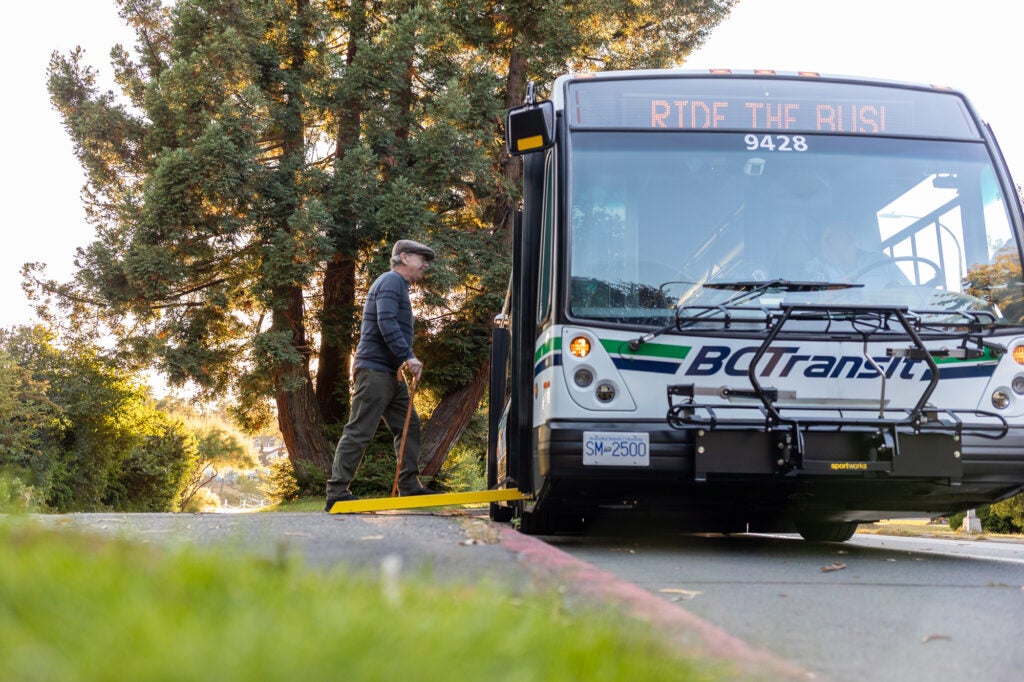 Accessibility bus stop with ramp deployed. Person walking with a cane into the bus.