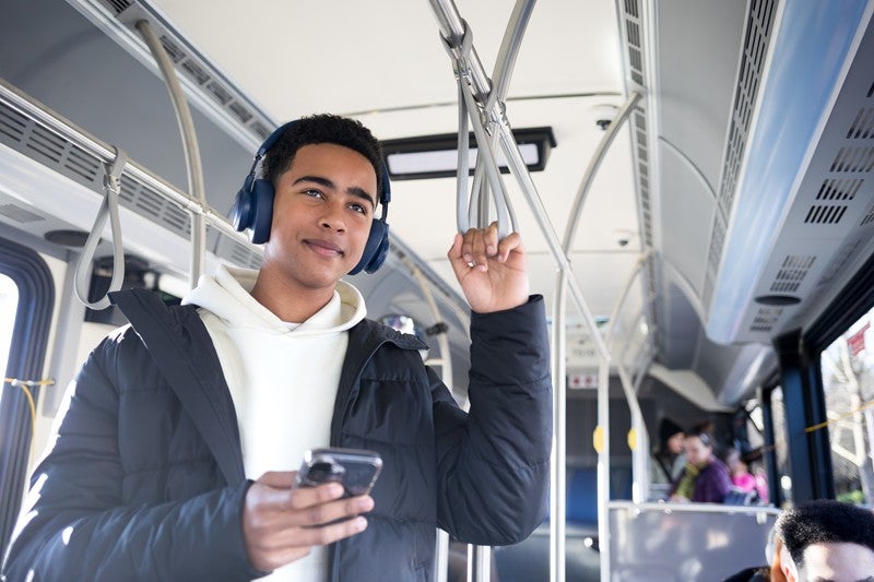 A young man on a bus, holding his phone in one hand and the bus hanging strap in his other hand.