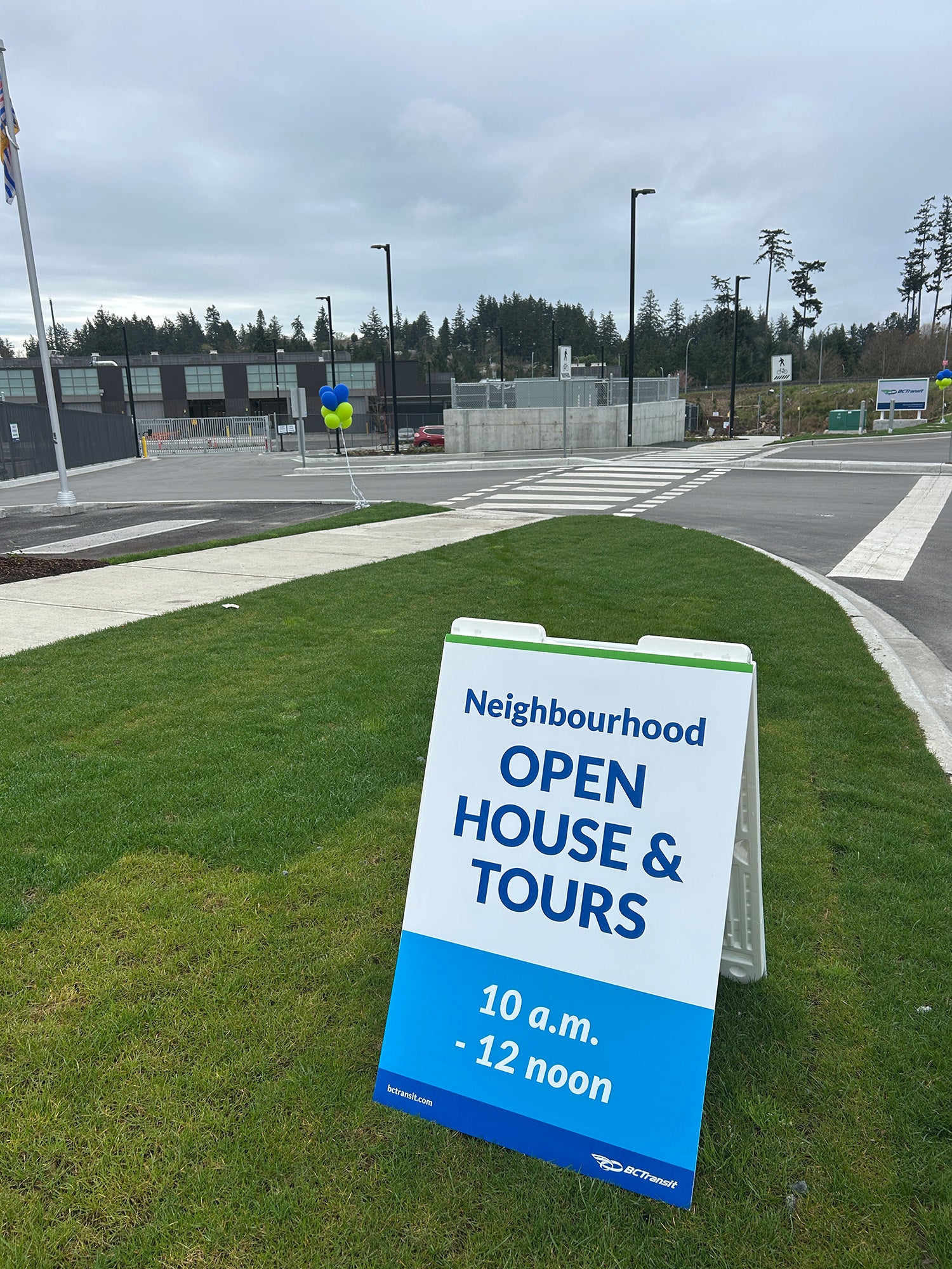 A sandwich board reading "Open house & Tours" on a grassy boulevard in front of the new Victoria handyDART Centre.