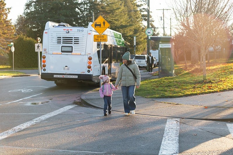 A parent and her child are walking away from a BC Transit bus.