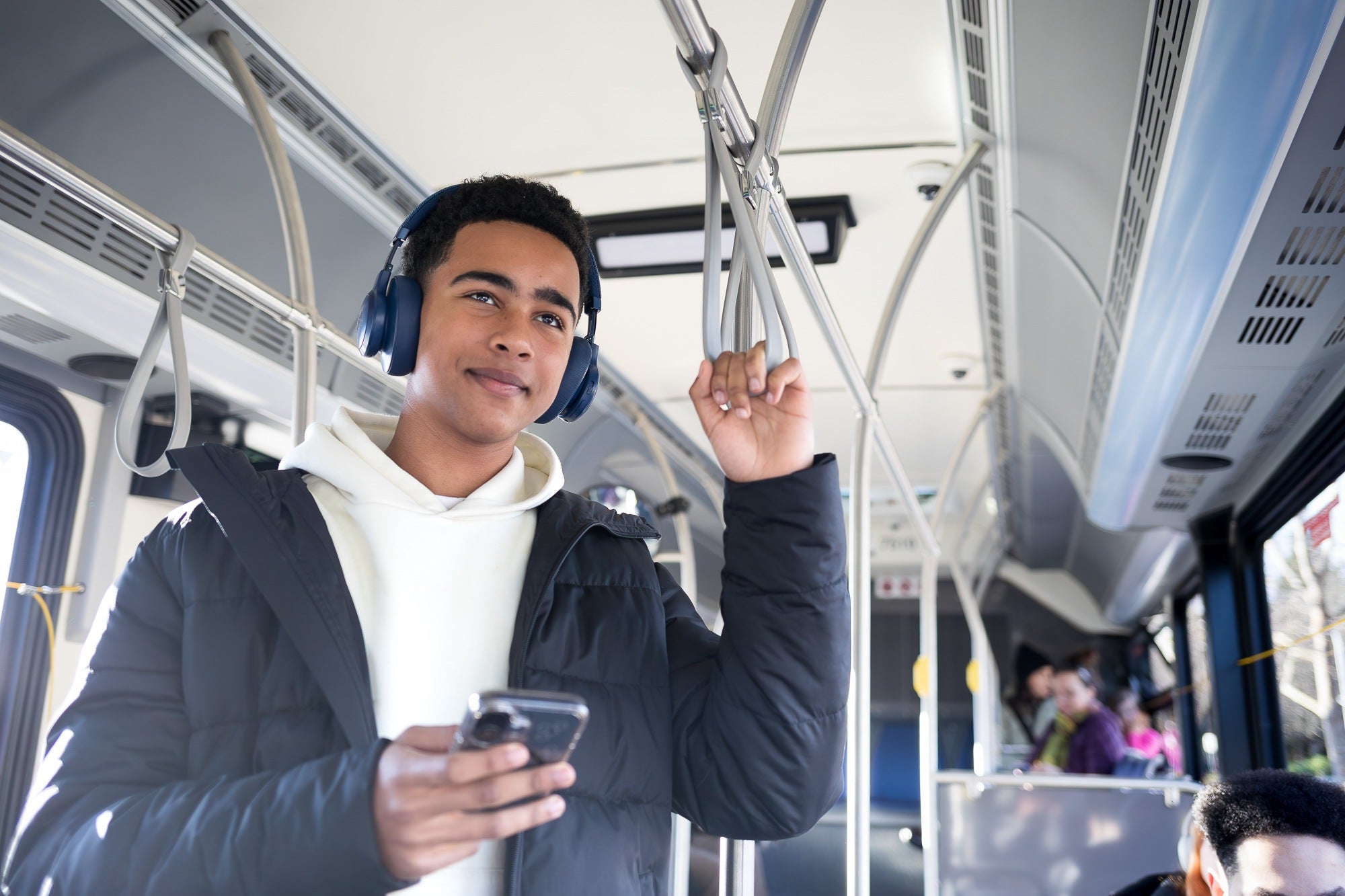 A young man on a bus, holding his phone in one hand and the bus hanging strap in his other hand.