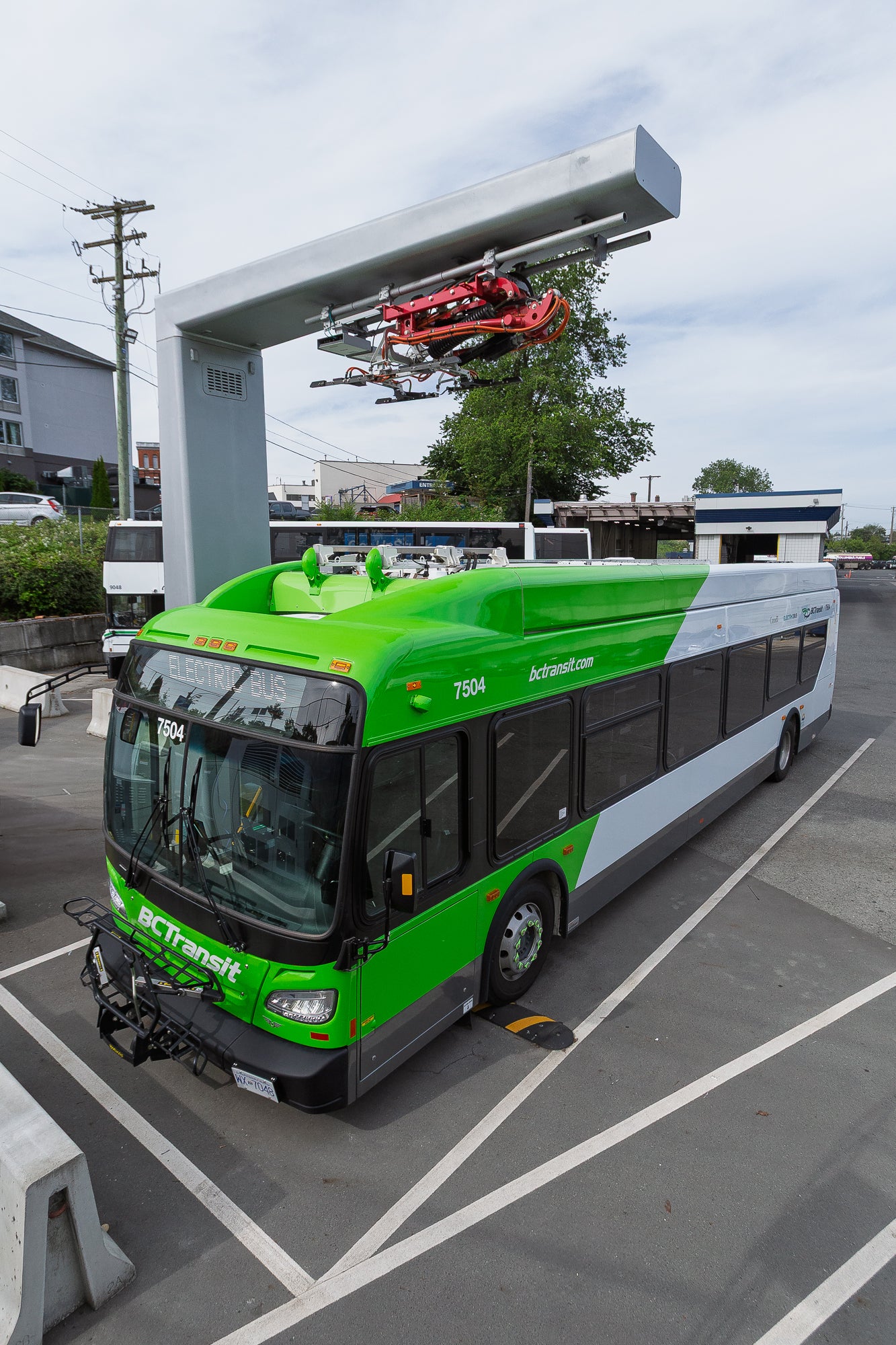 An electric bus parked beneath an overhead electric charger.