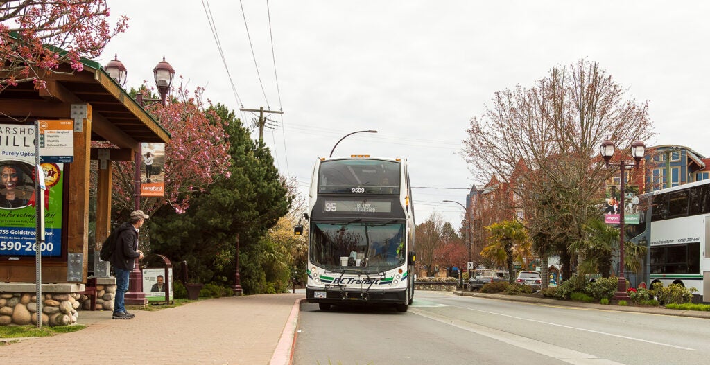 A double decker BC Transit bus pulling into a bus stop with orange Blink branded signage.