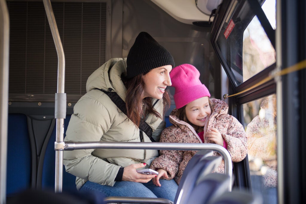A mother and her child are smiling and looking out the window on a bus.