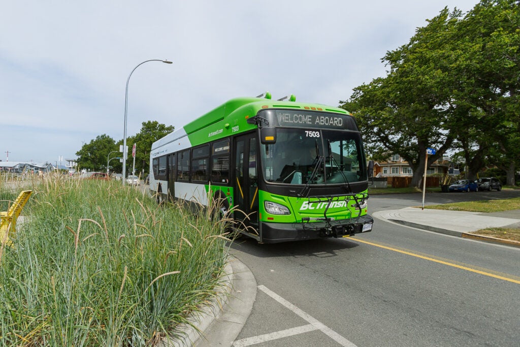A battery electric BC Transit bus drives past a grassy boulevard.