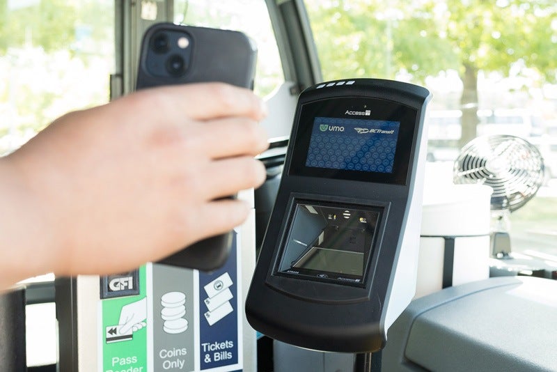 A phone being held up to a Umo fare validator at the front of a BC Transit bus.