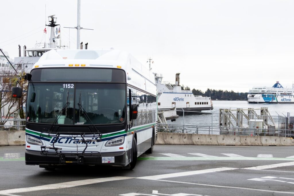 A BC Transit bus at a BC Ferries terminal, with two ferries behind.