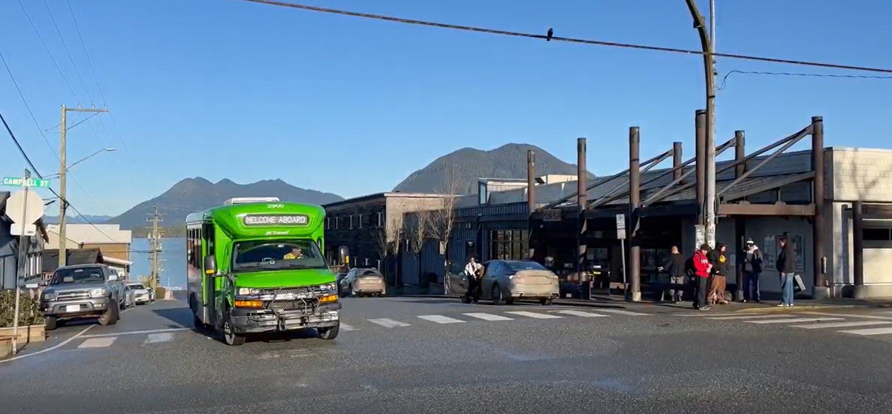 BC Transit bus turning left at an intersection in Tofino. The ocean and mountains are in the background.