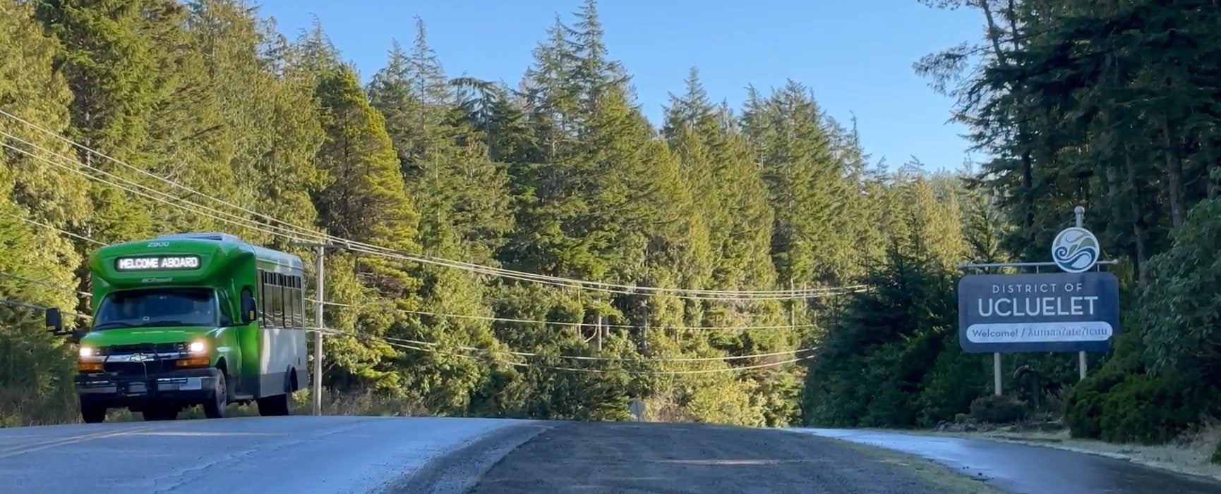 BC Transit bus on a highway, passing a sign that says "District of Ucluelet"
