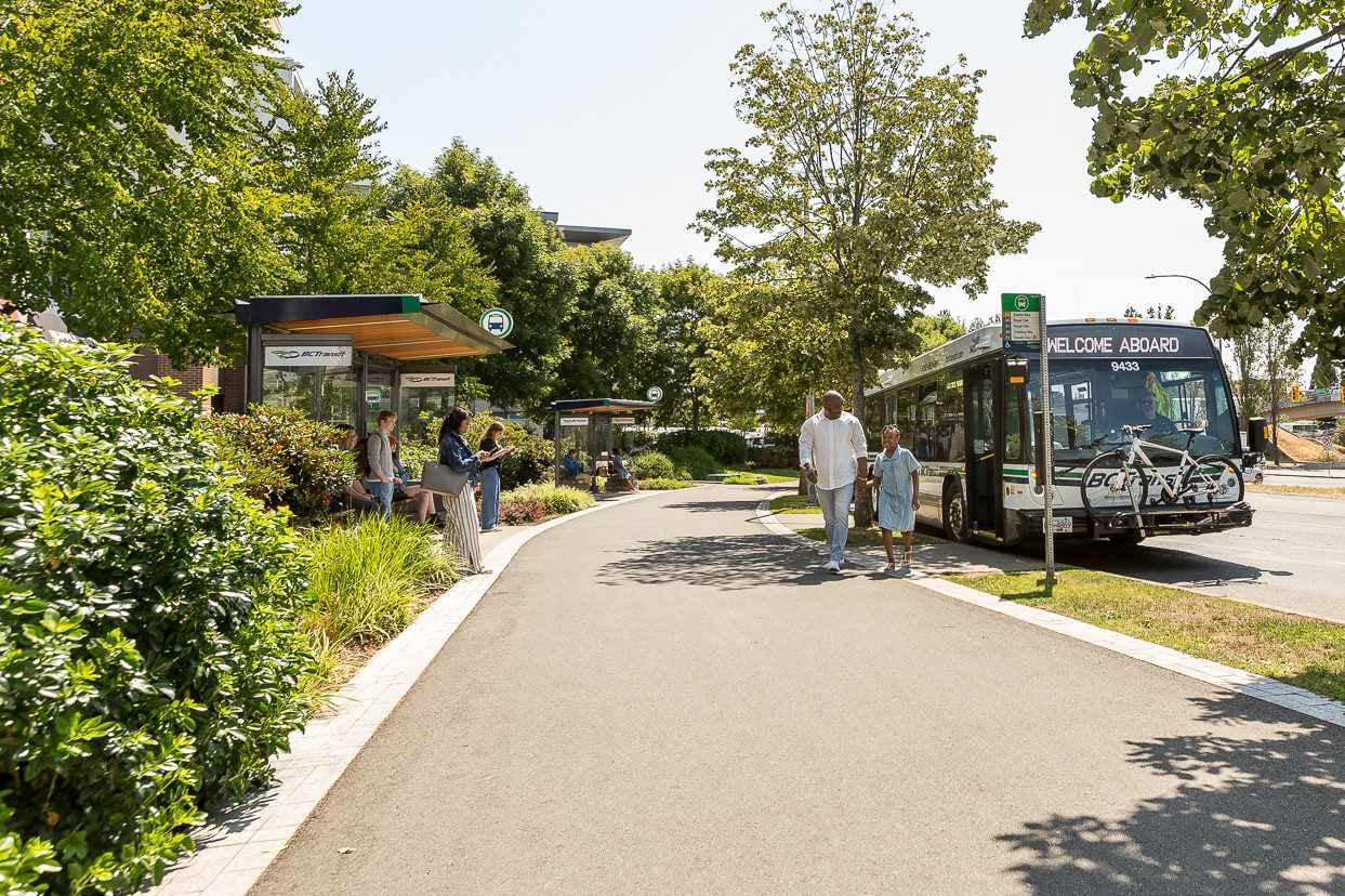 Two riders departing a stopped transit bus, while several more passengers wait at nearby transit shelters.