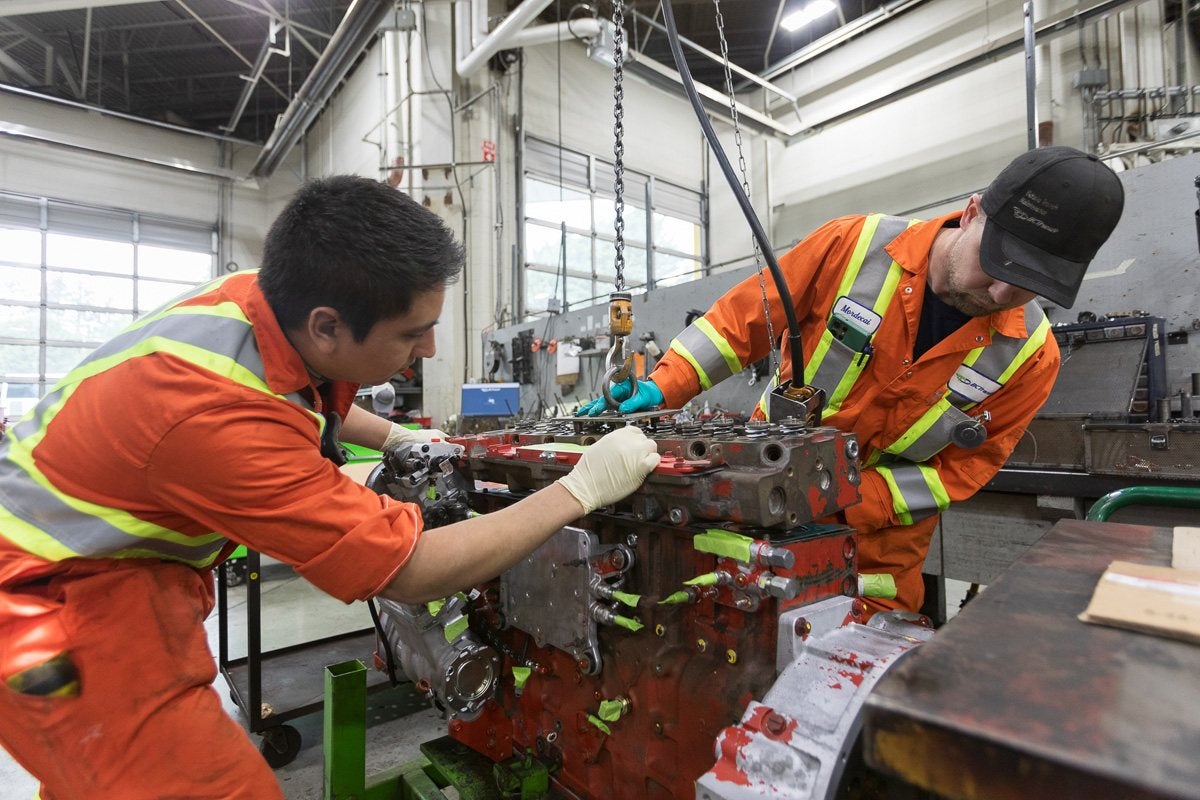 Two BC Transit mechanics working on an engine block in a maintenance bay.