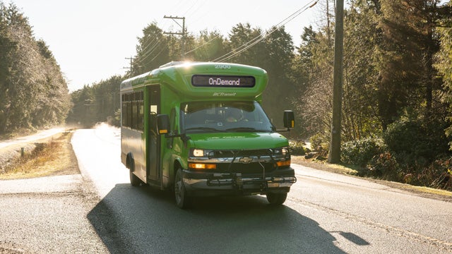 A BC Transit OnDemand bus on a rural road at sunrise.