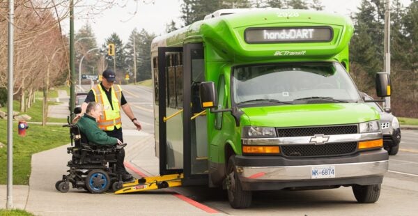 A driver helping a rider in a motorized wheelchair exit a handyDART bus.